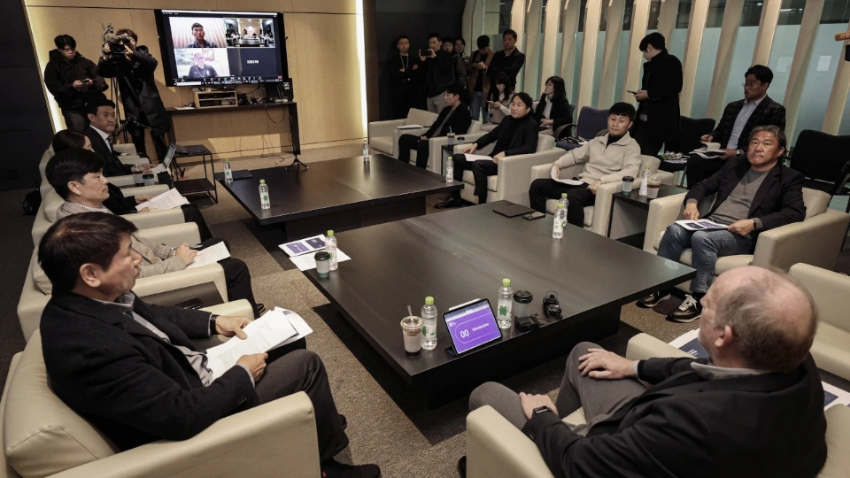 Группа мужчин сидит за столом, рядом их фотографируют