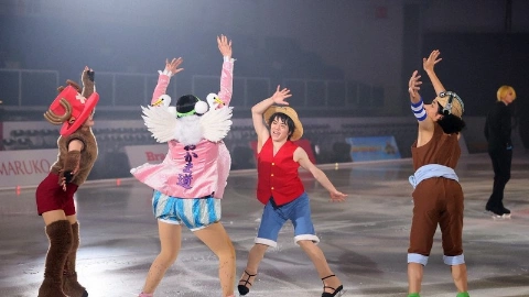 Юноша с чёрными волосами, в соломенной шляпе, в красной жилетке и синих шортах, танцует с другими актёрами на льду