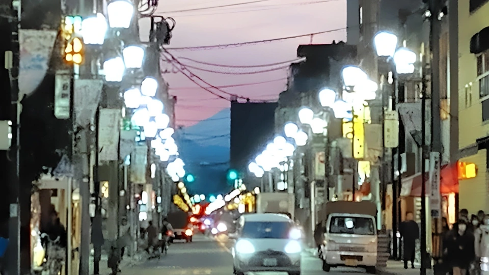 По дороге движется автомобиль, вдали видна гора, которую загораживает здание