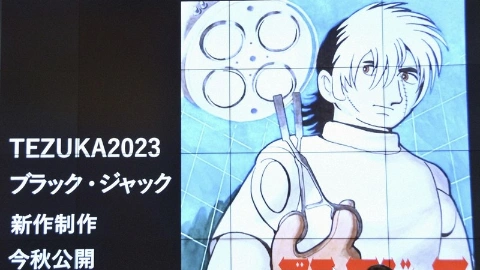 Мужчина и женщина сидят за столом перед микрофонами, позади изображение персонажа на большом экране