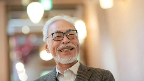 Мужчина с седыми белыми волосами, с седой бородой, в очках, в сером пиджаке, радостно улыбается, потирая руки