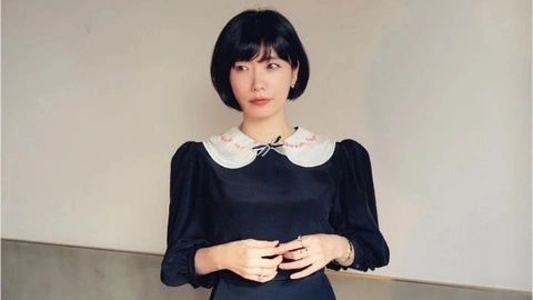 Девушка с чёрными волосами под «каре», с чёрными глазами, в длинном тёмно-синем платье с белым воротником, нервно соединяет пальцы рук