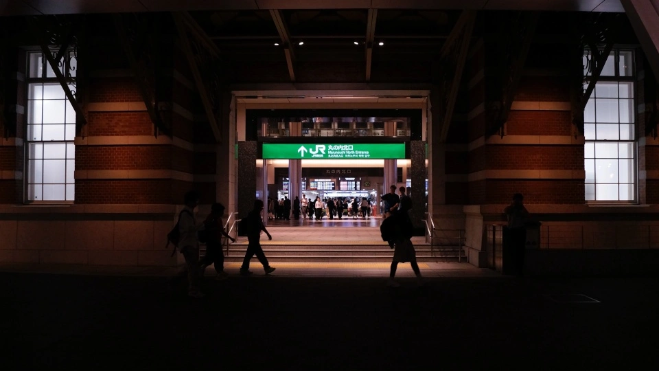 В ночи двое людей расходятся друг против друга, на заднем плане горит зелёная вывеска входа в метро Токио