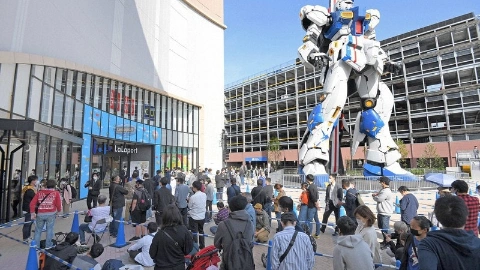 Огромный бело-синий робот стоит рядом со зданием, вокруг на него смотрят много людей