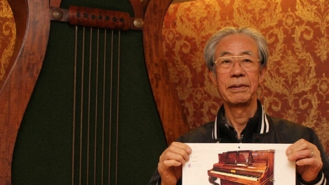 Пожилой седой мужчина в очках демонстрирует перед собой настенный календарь с изображением пианино, на заднем плане изображена арфа