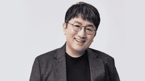 Мужчина с чёрными волосами, в очках, в деловом костюме, улыбается, убрав руку в карман брюк