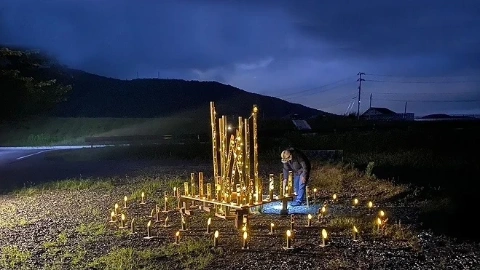 Человек в каске и на коленях, в ночи зажигает свечи